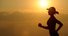 Gesundheitliche Aspekte beim Wodka Eine schwarze Silhouette einer Frau, die in einem dynamischen Laufstil vor einem leuchtend orangefarbenen Hintergrund rennt, während die Sonne direkt in die Kamera strahlt.