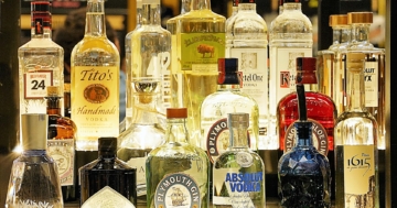 Mehrere Alkoholflaschen, darunter auch Wodkaflaschen, stehen hintereinander vor einem Spiegel, der die Flaschen reflektiert.