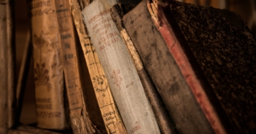 Mehrere alte Bücher, die nebeneinander auf einem Bücherregal stehen, symbolisieren die historische und etymologische Recherche über das Wort „Wodka“ / „Vodka“.